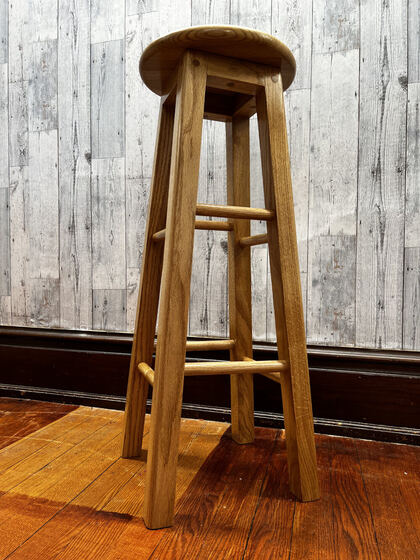 Single oak bar stool photographed low against a rustic wall