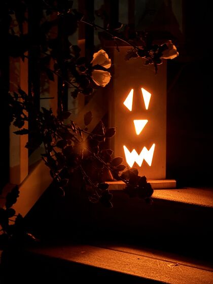 Ted's Halloween lantern — a large, bright, triangle-eyed jack-o'-lantern face carved in wood, glowing on porch steps